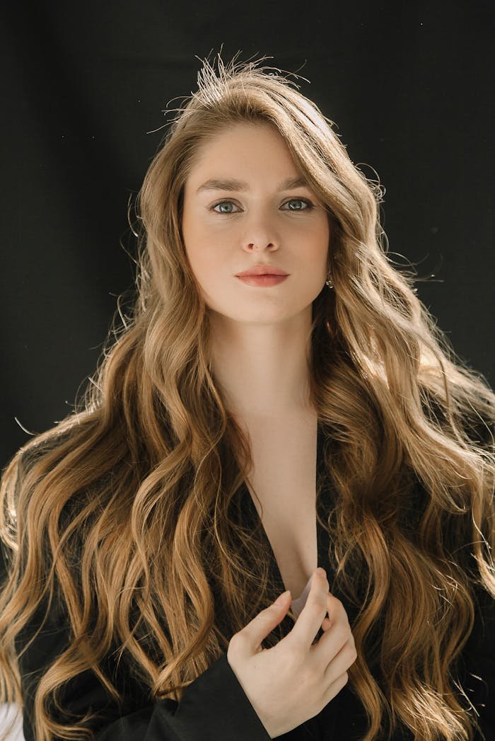 hero-gallery-03 Close-up portrait of a young woman with long, wavy blonde hair against a black background.